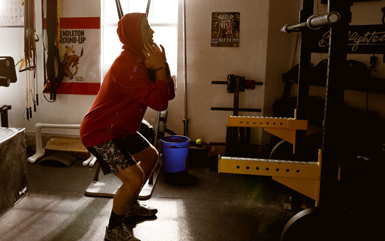 Foto de un hombre haciendo pesas en cuclillas en un gimnasio.